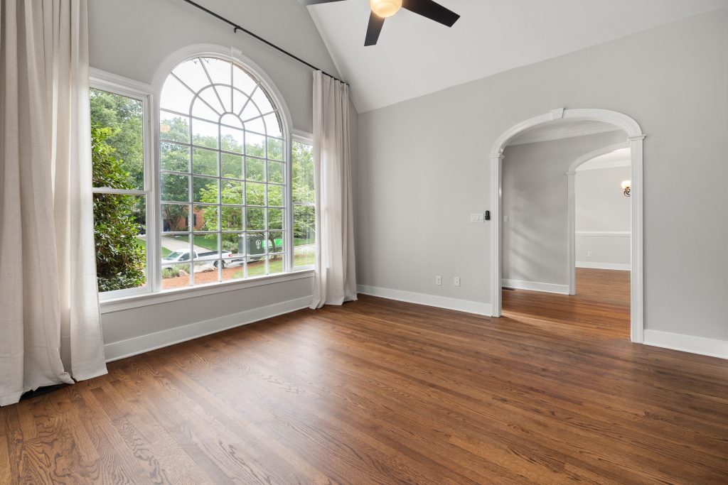 Modern empty living room featuring a large arched window and hardwood flooring.